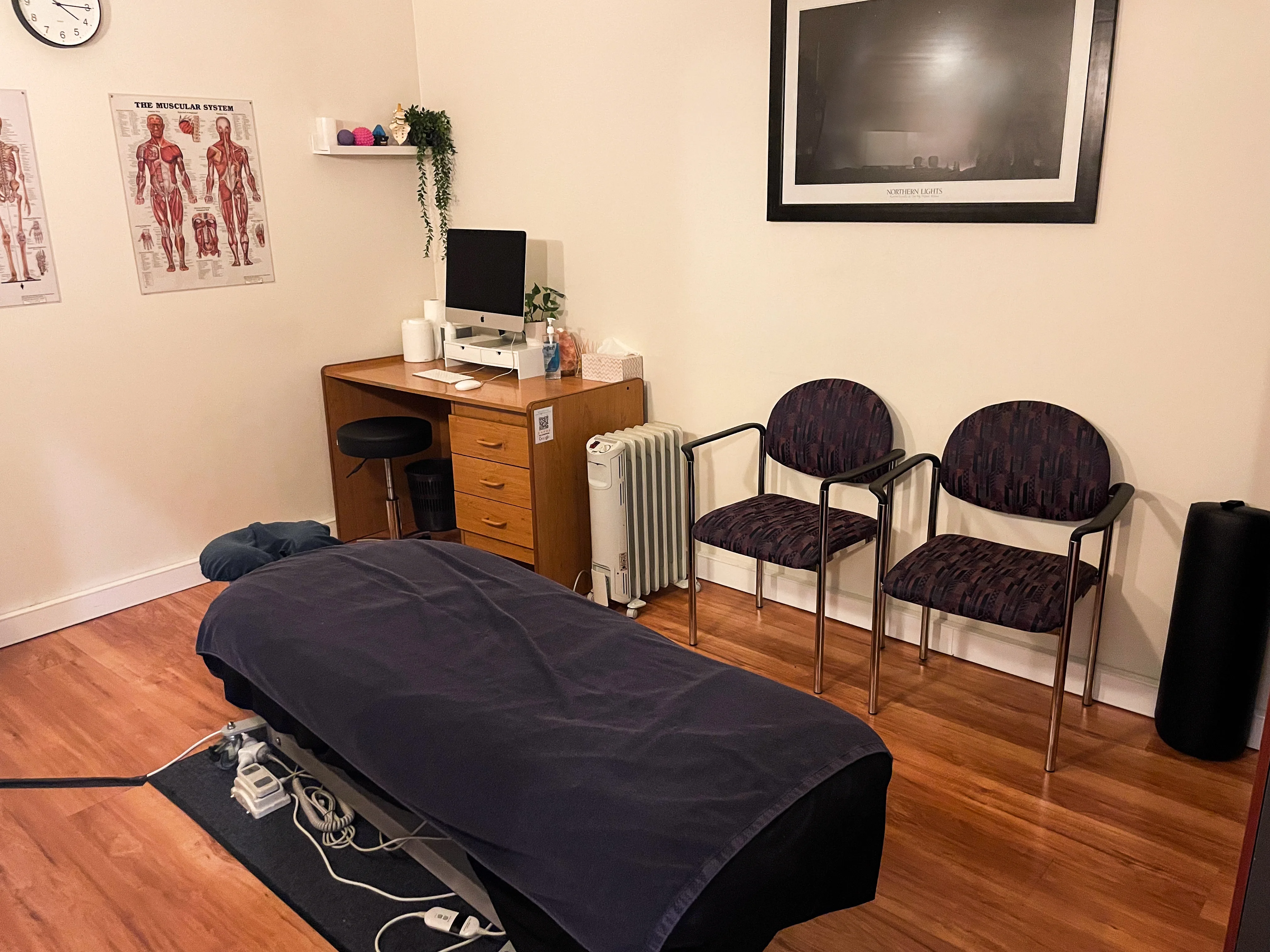 Treatment room at Brunswick Chiropractic — draped table, warm timber floor, anatomy posters
